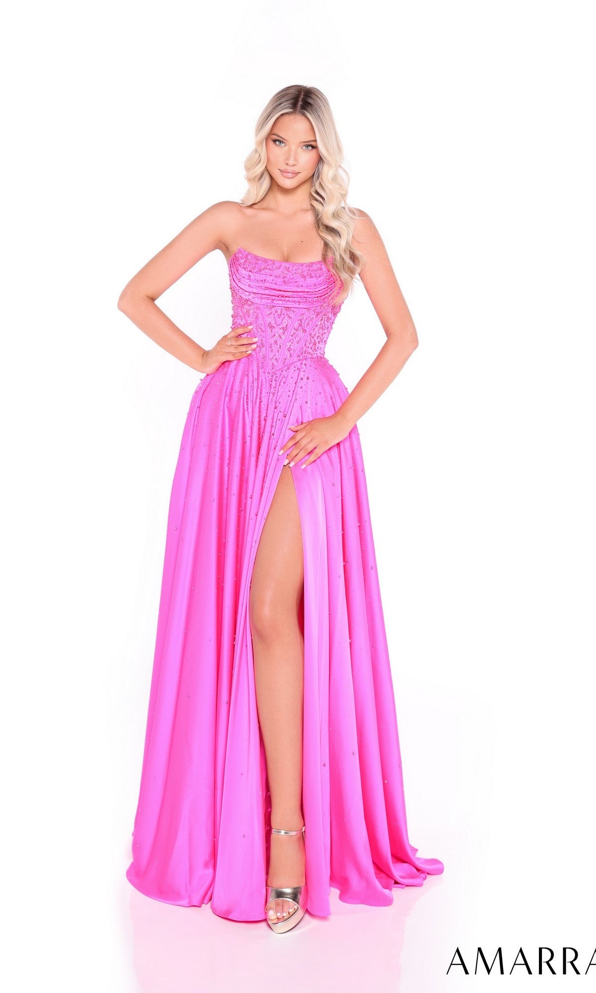 A woman stands against a white background wearing the Amarra 89387, a bright pink strapless satin prom dress featuring a high-leg slit and a rhinestone-embellished corset bodice.